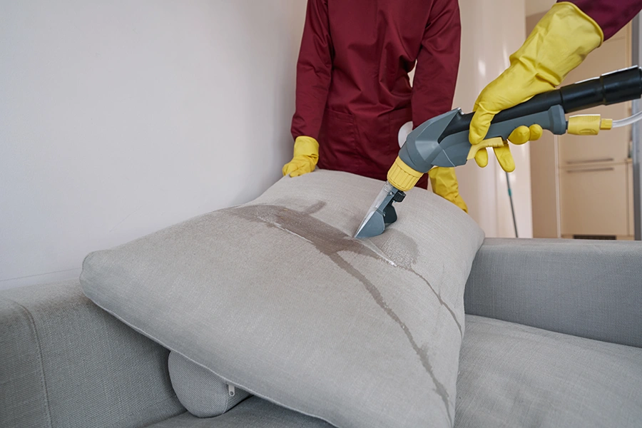 Two workers in rubber gloves steam-cleaning couch pillow