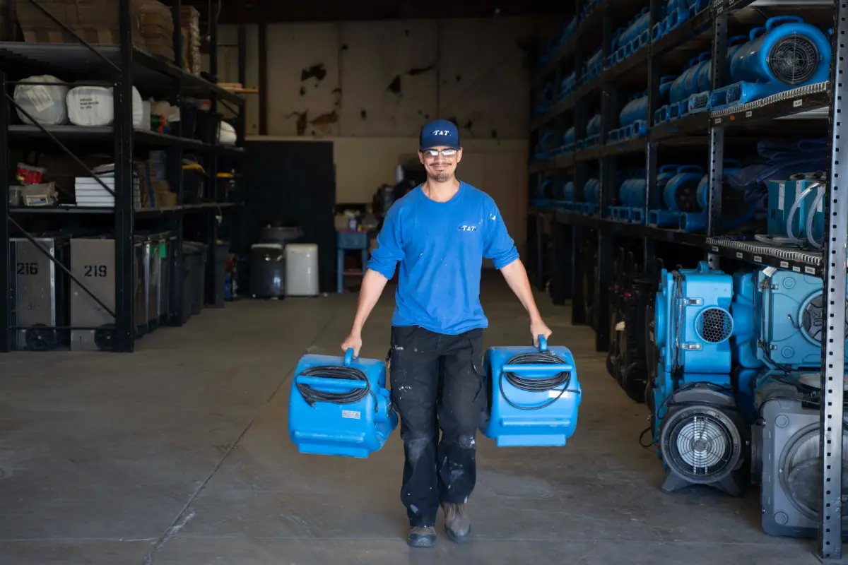 T&T technician carrying two air movers out of the Tucson warehouse to a job